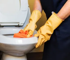 a person wearing yellow gloves is cleaning a toilet with an orange cloth .