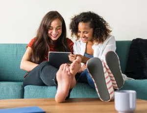 two women are sitting on a couch looking at a tablet