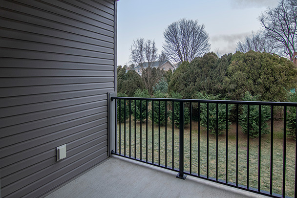 an empty balcony with a black railing and a view of trees