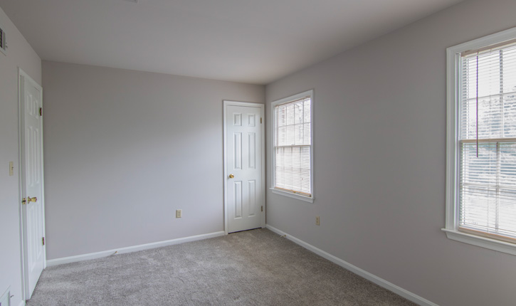 an empty bedroom with a door and two windows