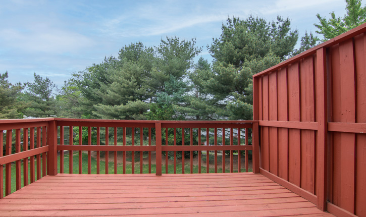 an empty deck with a red railing and trees in the background